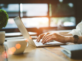 Closeup hands of Freelancer woman working using digital laptop computer and drink coffee breakfast on workplace table at cafe shop in the morning.