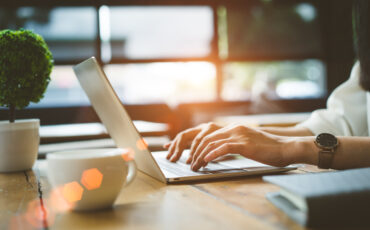 Closeup hands of Freelancer woman working using digital laptop computer and drink coffee breakfast on workplace table at cafe shop in the morning.